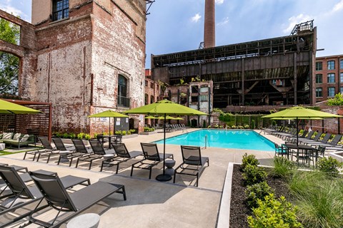 a swimming pool with chaise lounge chairs and umbrellas in front of a brick building