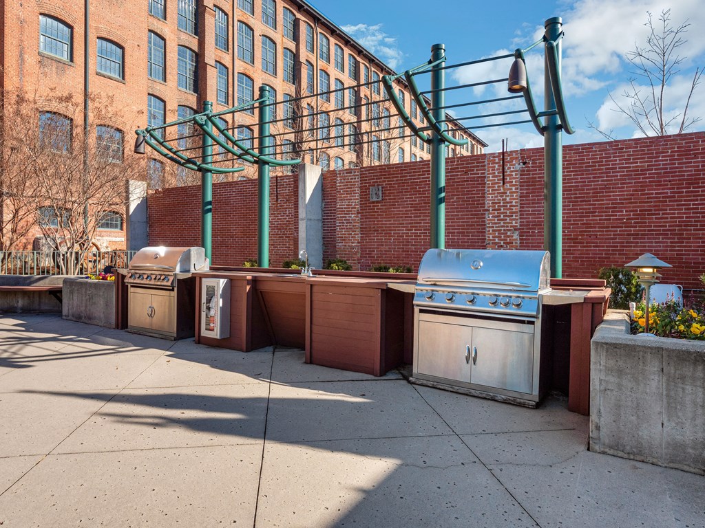 a row of barbecue pits on a sidewalk in front of a brick building
