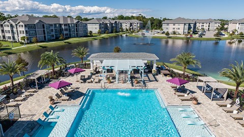 A large swimming pool with loungers and umbrellas in front of a resort.