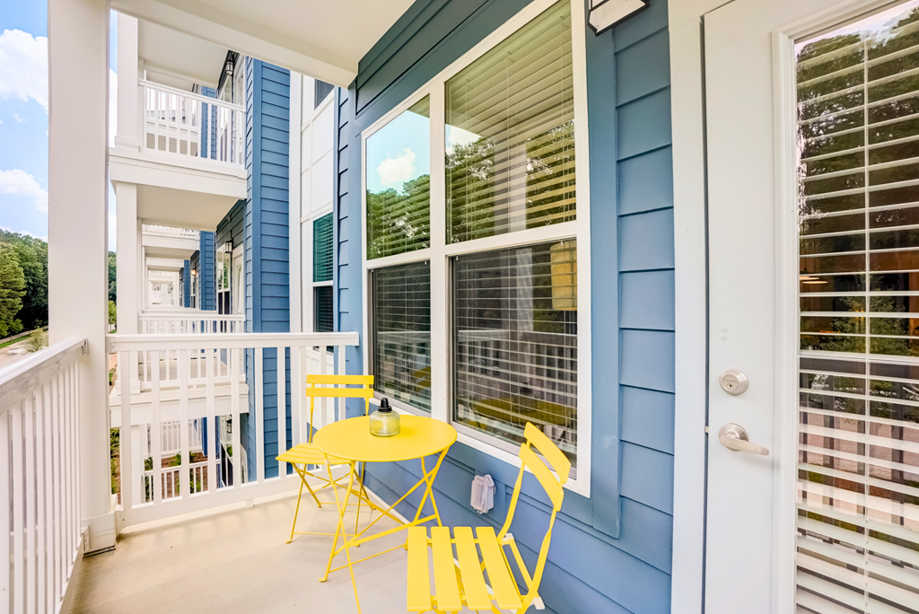 a small yellow table and two yellow chairs sit on the porch of a blue house