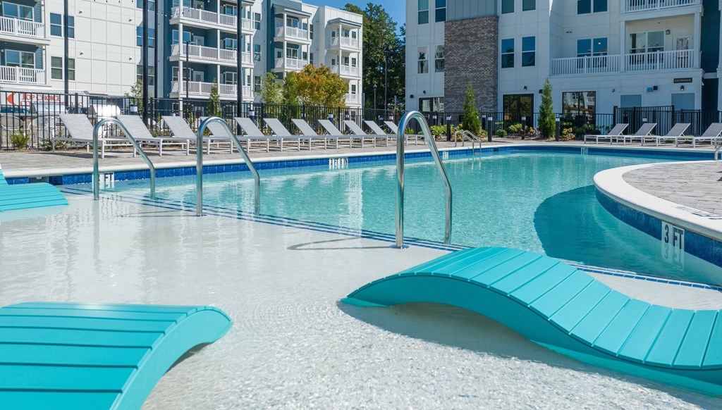 a swimming pool with blue lounge chairs in front of an apartment building