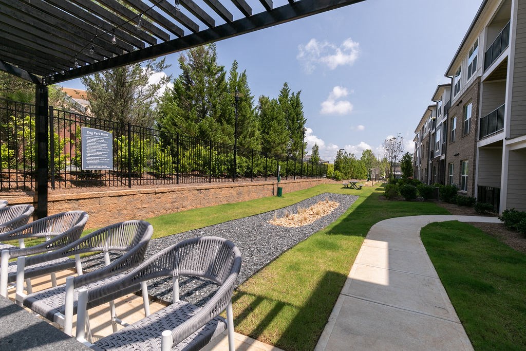 a patio with chairs and grass and trees in front of an apartment building