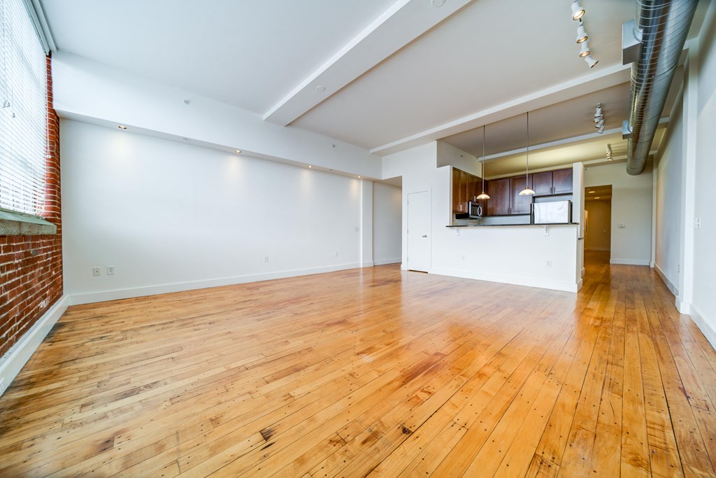 an empty living room with wood floors and a kitchen
