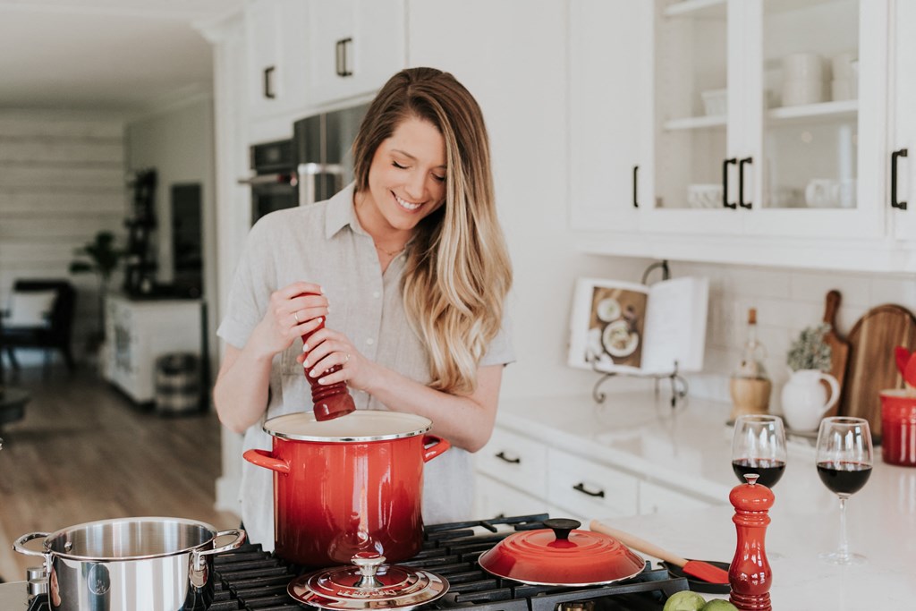 a woman in a kitchen stirring a pot with a striped measuring cup