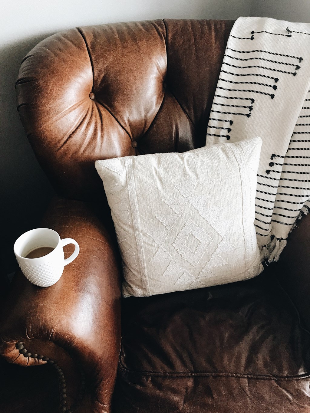 a cup of coffee and a pillow on a leather chair