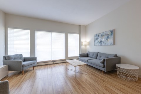 A living room with a grey couch, a chair, a table, and a painting on the wall.
