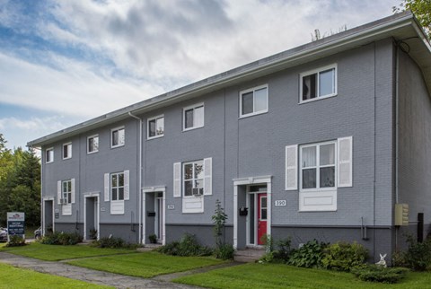 a gray building with a red door and a lawn