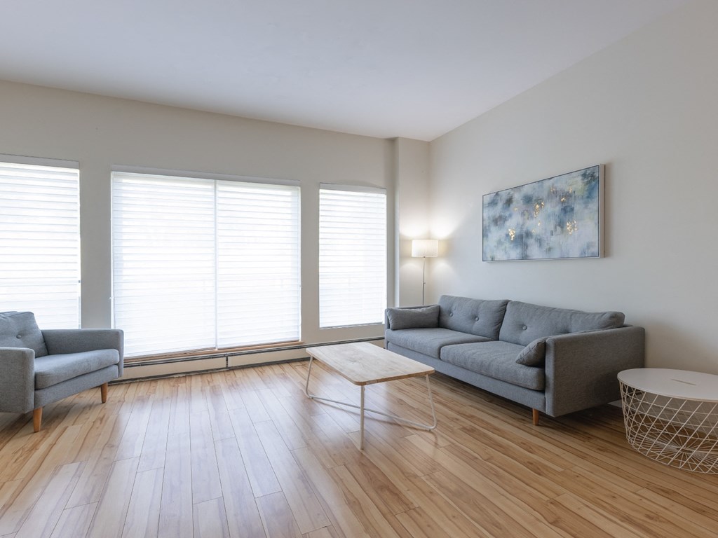 A living room with a grey sofa, a grey armchair, a white coffee table, and a painting on the wall.