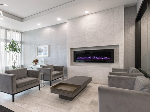 A modern living room with grey furniture and a purple lighted fireplace.