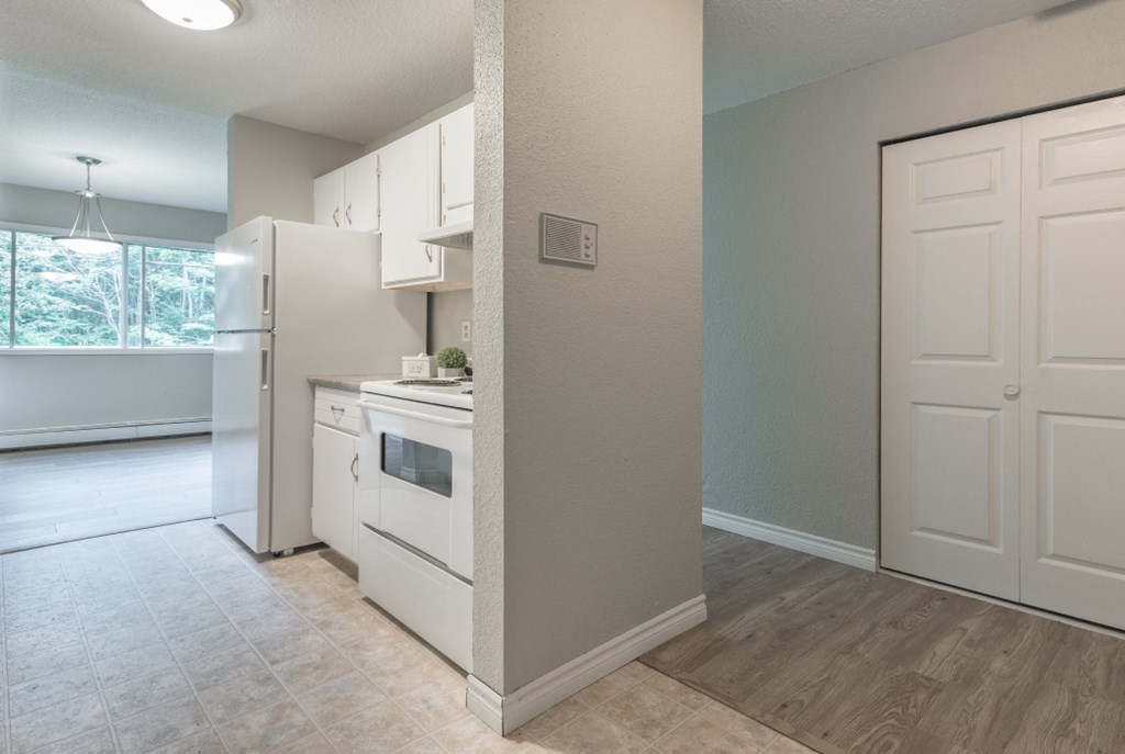 an empty kitchen with white appliances and a door to the living room