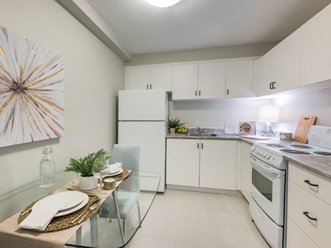 A modern kitchen with white cabinets and a glass table.