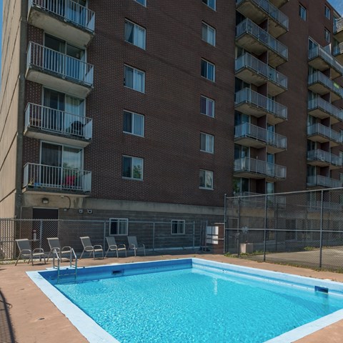 A pool in front of a red brick building with balconies.