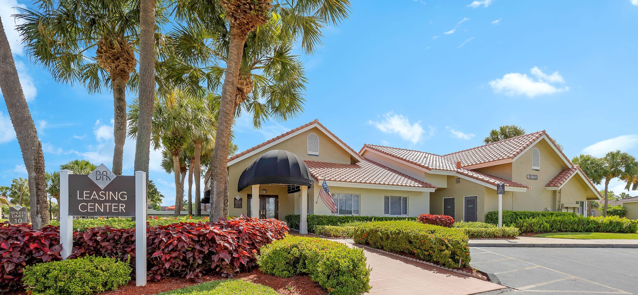 a leasing center sign in front of a yellow house with palm trees