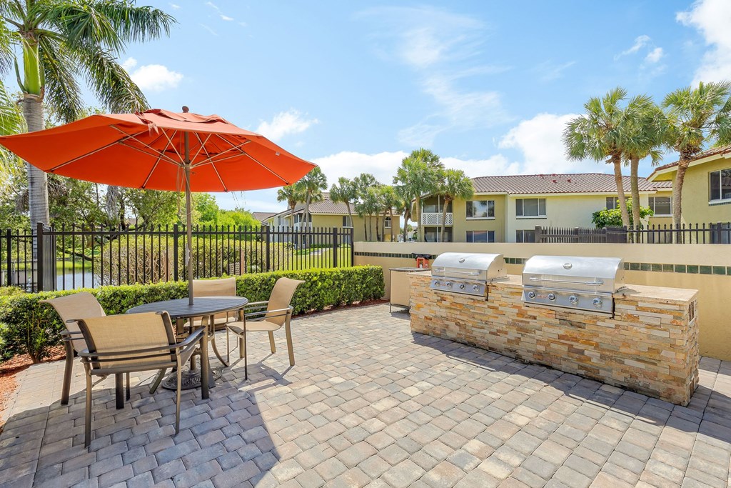 a patio with a grill and a table with chairs and an umbrella