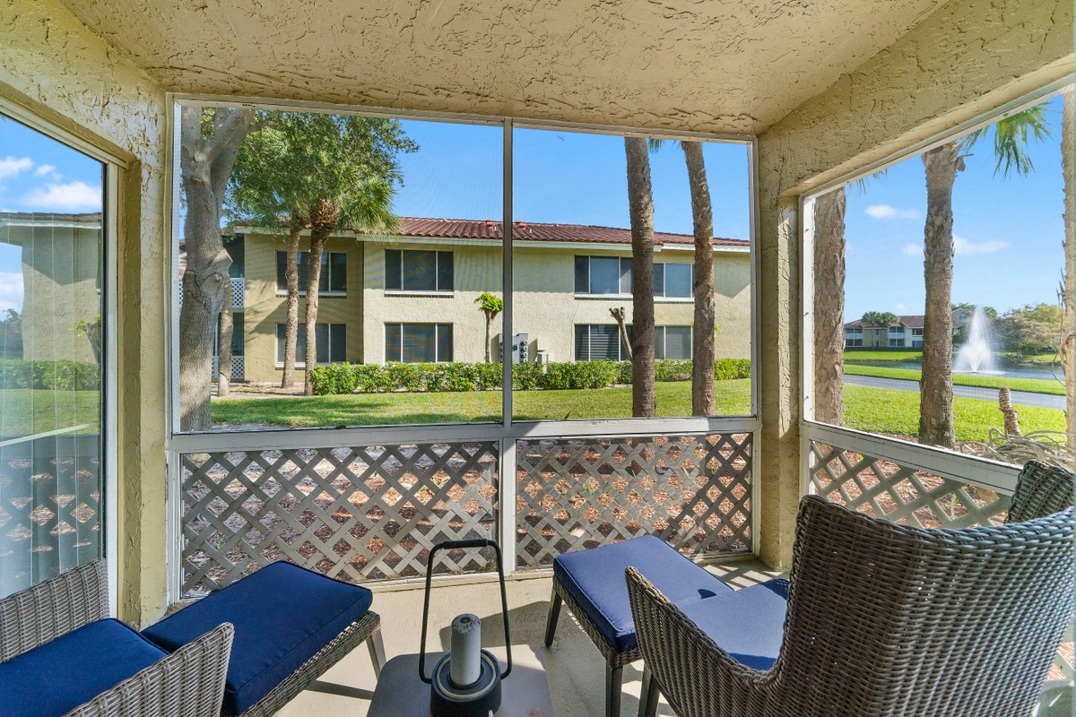 Patio with two chairs and table looking at exterior of aartment building and lake with fountain