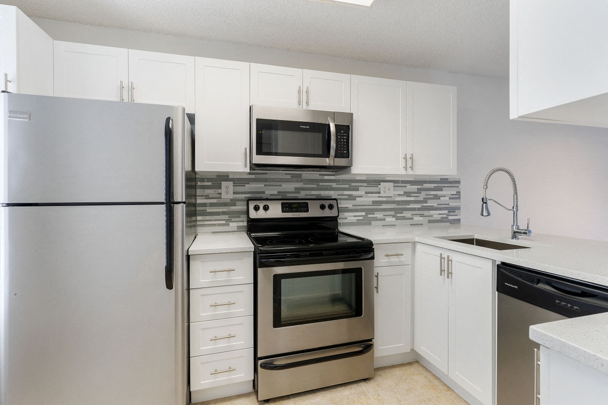 Kitchen with cabinets, sink with vegetable sprayer, tile back splash, stainless steel oven, microwave, and refrigerator, and dishwasher.