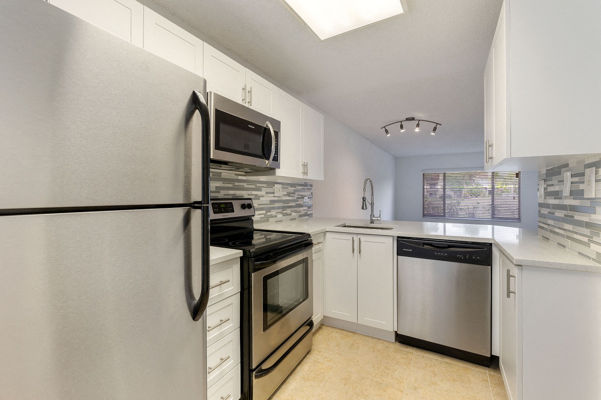 Kitchen with cabinets, sink with vegetable sprayer, tile back splash, stainless steel oven, microwave, and refrigerator, and dishwasher.