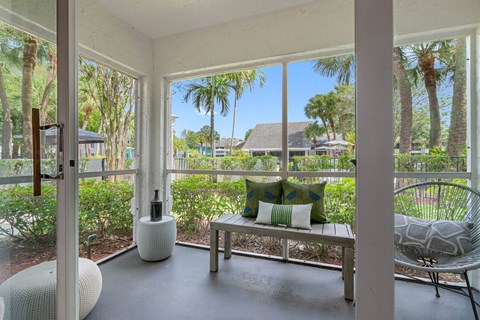 a screened porch with a bench and chairs and a view of palm trees