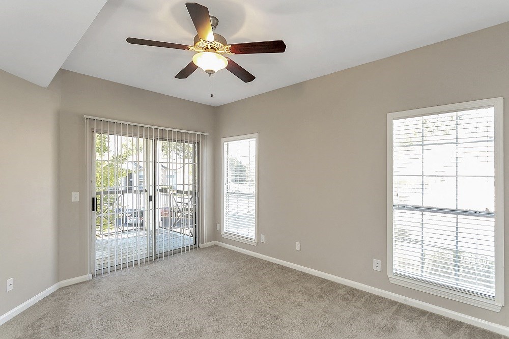 an empty living room with a ceiling fan and a door to a balcony