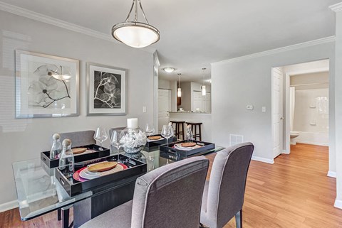Aurora, IL, Townhomes - The Apartments at Kirkland Crossing - Dining Area With Glass Table, Upholstered Chairs, Pendant Light, Open Kitchen Breakfast Bar, And Wood Floors.