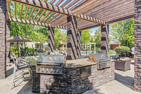 Townhomes In Aurora, IL - The Apartments At Kirkland Crossing - Covered Grill Area With Two BBQs, Trees, Counterspace With Bar Chairs.