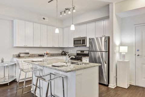 Vernon Hills, IL Apartments - Designer Kitchens With Breakfast Bar, Granite Countertops. White Cabinetry, Wood-Style Flooring, And Stainless Steel Appliances.
