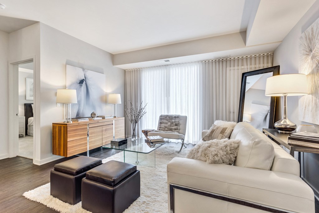 Vernon Hills, IL Apartments - The Oaks of Vernon Hills - Large Living Room With High Ceilings, Wood-Inspired Plank Flooring, Area Rug, Couch, Chair, Stools, And Access To Patio Or Balcony Area Via Sliding Glass Door