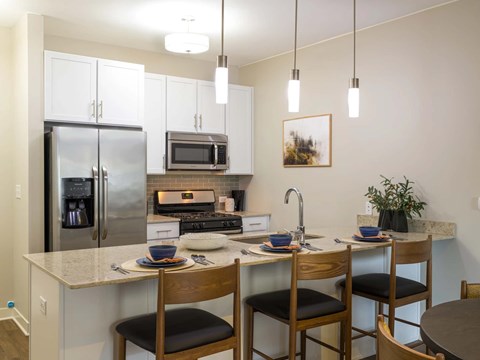 A kitchen with a refrigerator, microwave, oven, sink, and a dining table with chairs.