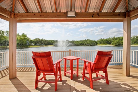 A wooden deck with red chairs and a table overlooking a lake.