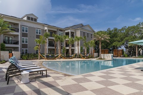 A large swimming pool is surrounded by a tiled patio and lounge chairs.