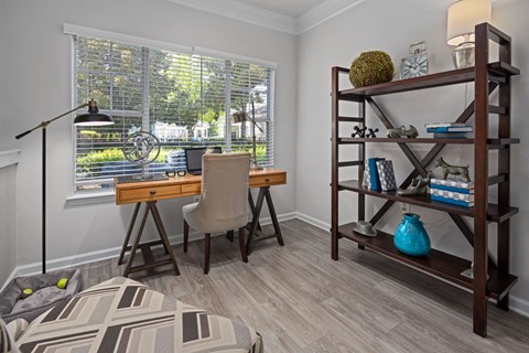 A room with a desk, chair, and a shelf with various items.