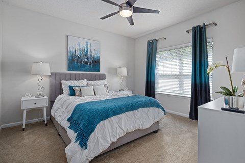 A bedroom with a bed, a ceiling fan, and a painting on the wall.