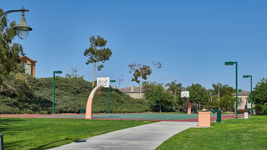 A park with a basketball court and a green lamp post.