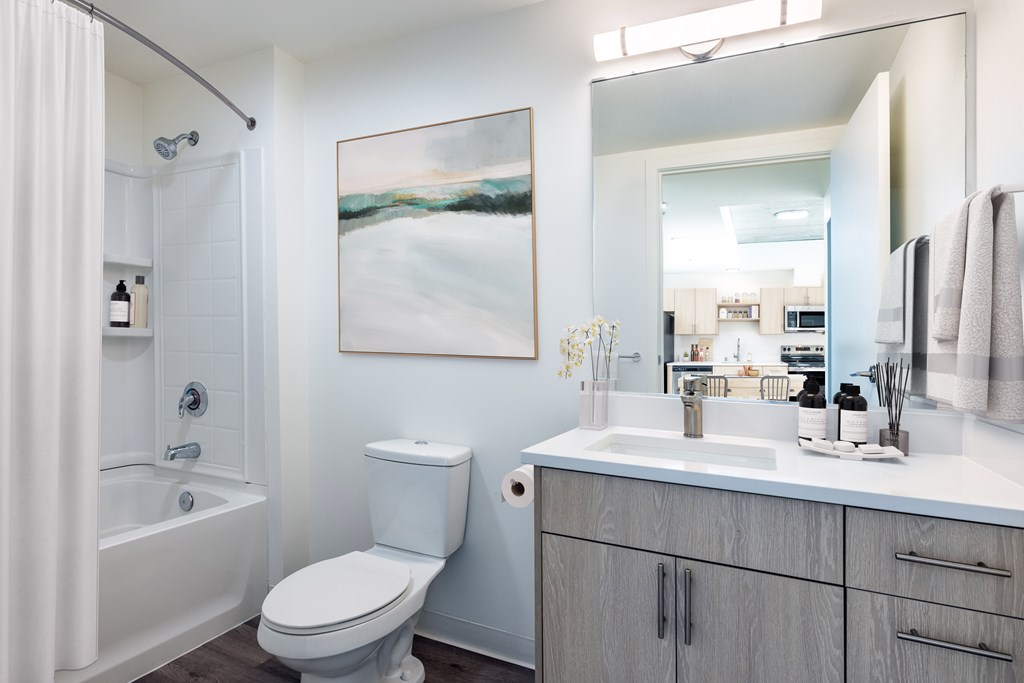 A bathroom with a white toilet, a white sink, and a large painting on the wall.