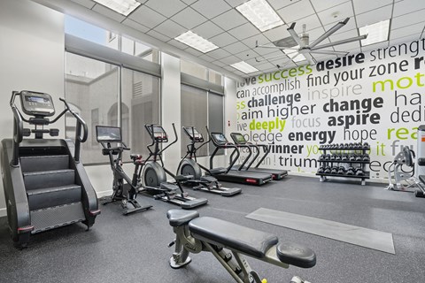 A gym with a variety of equipment and a motivational word cloud on the wall.