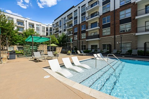A swimming pool surrounded by lounge chairs and apartment buildings.