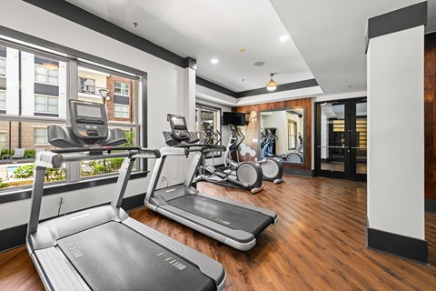 A treadmill in a gym with a view of a building outside the window.