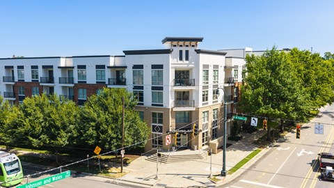 A street view of a city with a green bus on the left and a white building with a balcony on the right.