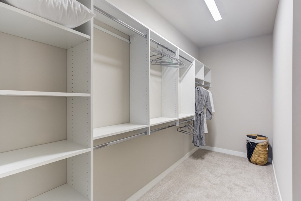 a walk in closet with white shelving and a basket on the floor