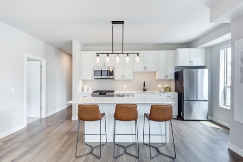 A kitchen with white cabinets and a white island with three barstools.
