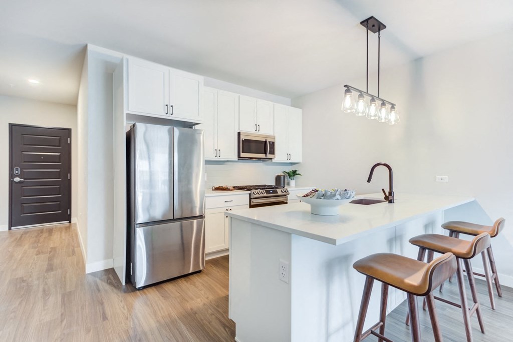 a kitchen with a large island with stools and a stainless steel refrigerator