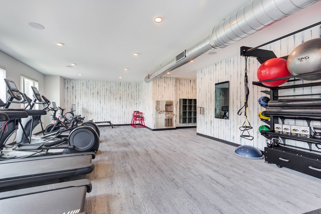 the gym with treadmills and weights in a room with white walls and wood