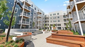 A modern apartment complex with a spacious courtyard and wooden benches.