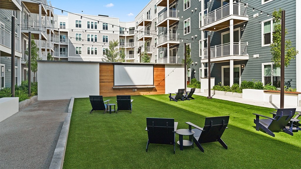 A modern outdoor seating area with black chairs and tables is surrounded by apartment buildings.