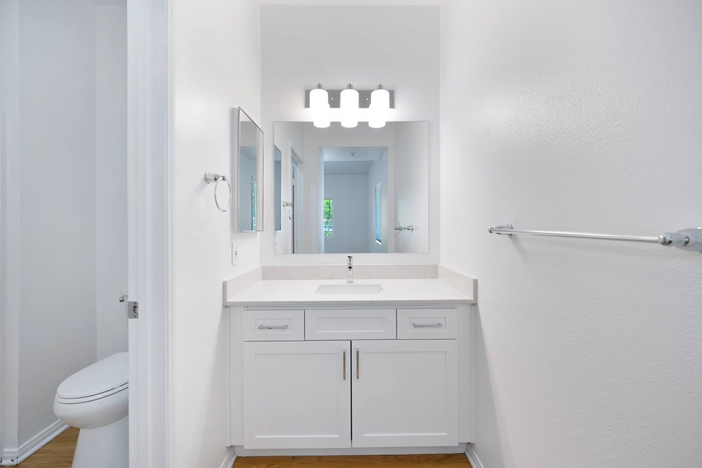 A white bathroom with a sink, mirror, and toilet.