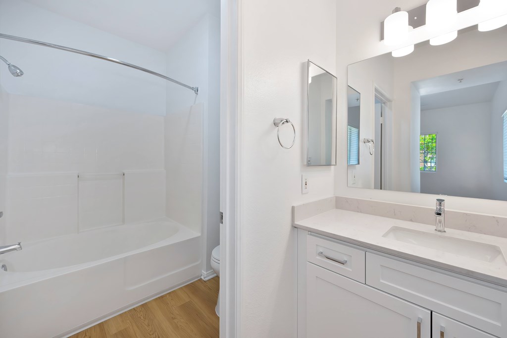 A white bathroom with a white tub, sink, and mirror.