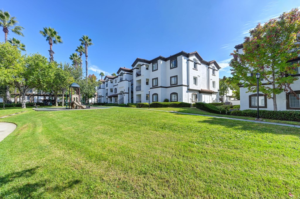 A large white building with a black roof is surrounded by a green lawn and palm trees.