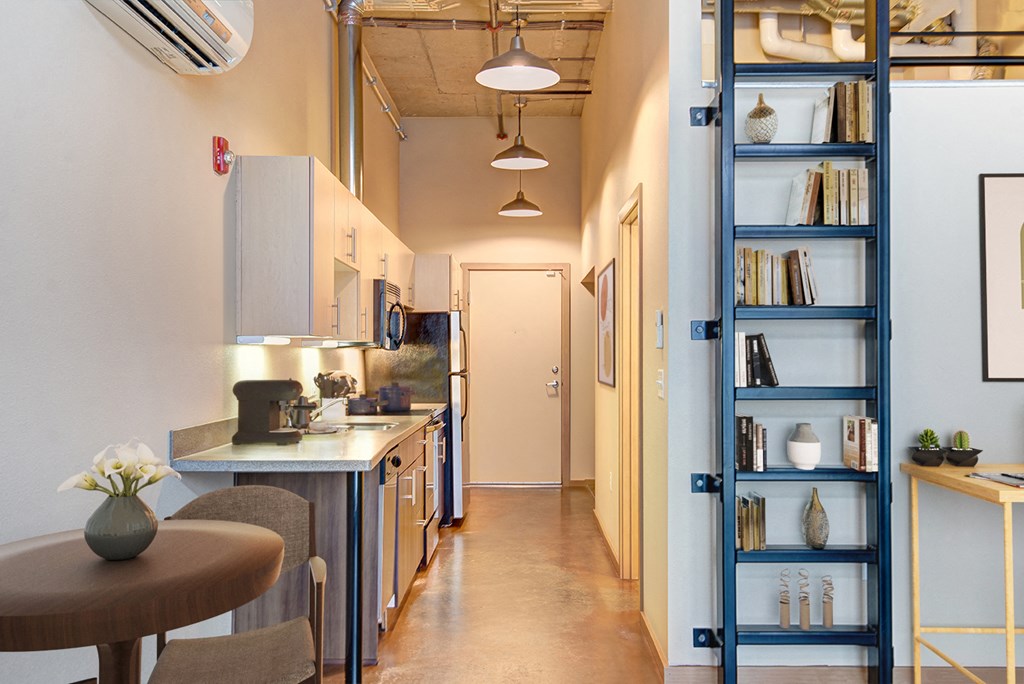 A kitchen with a table and a shelf with books and vases.