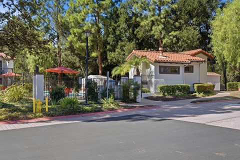 A house with a red roof is surrounded by trees and a fence.