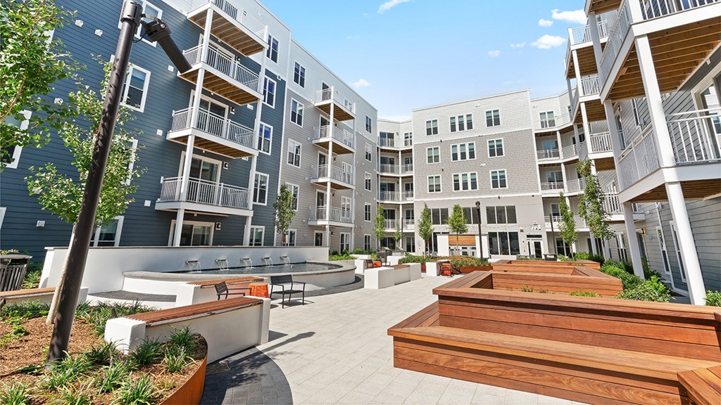 A modern apartment complex with a spacious courtyard and wooden benches.
